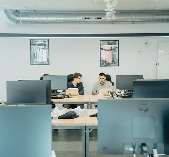 Two people at neighbouring desks, mid conversation